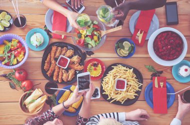 Ahşap masada otururken birlikte yemek yiyen bir grup insanın üst düzey görüntüsü. Masada yemek var. İnsanlar fast food yiyor..