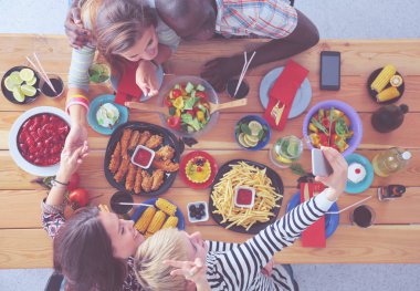 Ahşap masada otururken birlikte yemek yiyen bir grup insanın üst düzey görüntüsü. Masada yemek var. İnsanlar fast food yiyor..