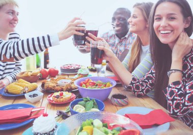 Ahşap masada otururken birlikte yemek yiyen bir grup insanın üst düzey görüntüsü. Masada yemek var. İnsanlar fast food yiyor..