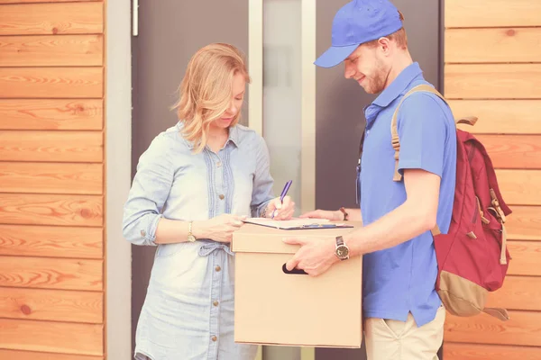 Repartidor sonriente con uniforme azul que entrega la caja de paquetes al destinatario: concepto de servicio de mensajería. Repartidor sonriente en uniforme azul — Foto de Stock