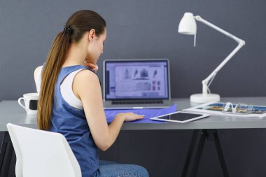 Masasında enstrümanlar, planlar ve dizüstü bilgisayarlarla oturan genç bir kadın..