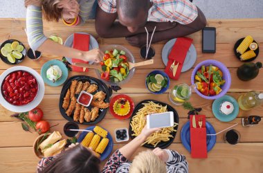 Ahşap masada otururken birlikte yemek yiyen bir grup insanın üst düzey görüntüsü. Masada yemek var. İnsanlar fast food yiyor..