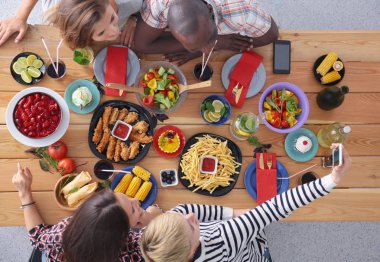 Ahşap masada otururken birlikte yemek yiyen bir grup insanın üst düzey görüntüsü. Masada yemek var. İnsanlar fast food yiyor..