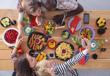 Ahşap masada otururken birlikte yemek yiyen bir grup insanın üst düzey görüntüsü. Masada yemek var. İnsanlar fast food yiyor..