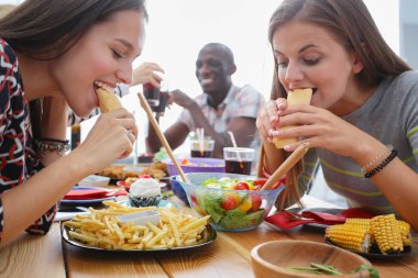 Ahşap masada otururken birlikte yemek yiyen bir grup insanın üst düzey görüntüsü. Masada yemek var. İnsanlar fast food yiyor..