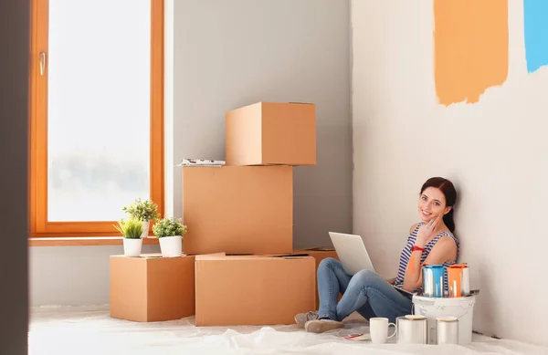 Portret van de jonge vrouw tijdens het schilderen van nieuw appartement, zitten met laptop. Jonge vrouw met laptop — Stockfoto