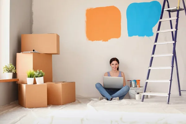 Portret van de jonge vrouw tijdens het schilderen van nieuw appartement, zitten met laptop. Jonge vrouw met laptop — Stockfoto
