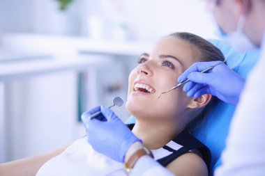 Dişçi muayenehanesinde diş muayenesi yapan ağzı açık genç bir kadın hasta..