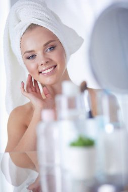 Bornozlu genç kadın banyo aynasına bakıyor.