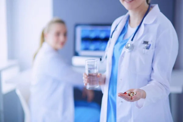Lövés orvos gazdaság tabletták és pohár víz a klinikán kollégával a háttérben. — Stock Fotó