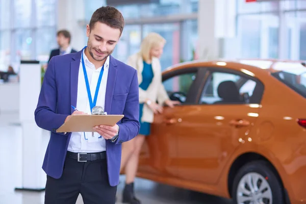 Vendedor fica perto de um carro novo no showroom — Fotografia de Stock