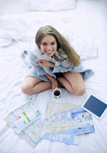 Relaxado jovem mulher sentada na cama com uma xícara de café e tablet digital — Fotografia de Stock