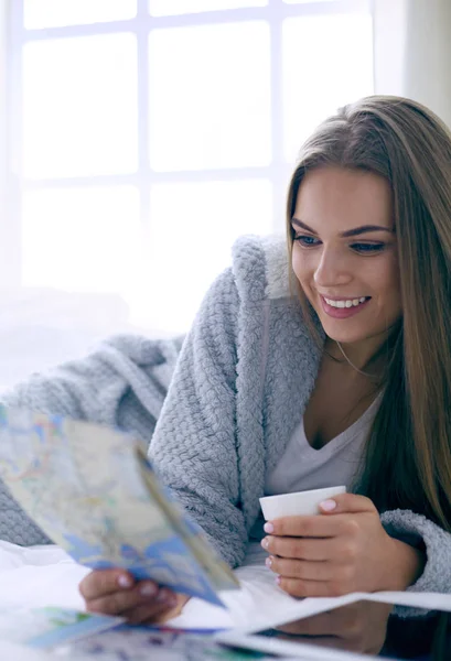 Relaxado jovem mulher sentada na cama com uma xícara de café e tablet digital — Fotografia de Stock