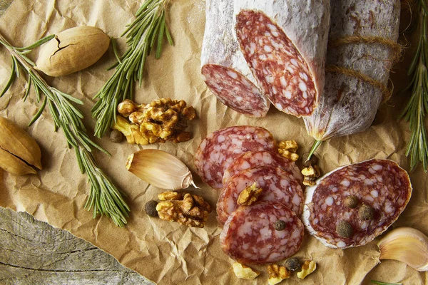 Italienische Salami mit Meersalz, Rosmarin, Knoblauch und Nüssen auf Papier. Rustikaler Stil. Nahaufnahme. — Stockfoto