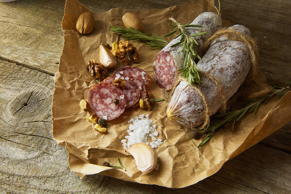 Italian salami wih sea salt, rosemary, garlic and nuts on paper. Rustic style. Top view.
