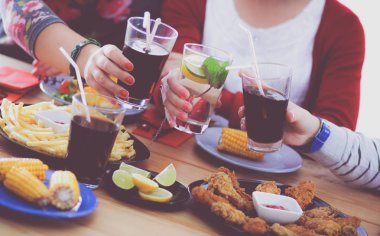 Ahşap masada otururken birlikte yemek yiyen bir grup insanın üst düzey görüntüsü. Masada yemek var. İnsanlar fast food yiyor..
