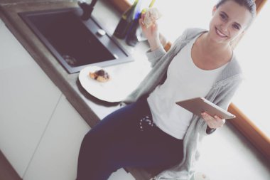 Mutfakta dijital tablet kullanan güzel genç bir kadın..