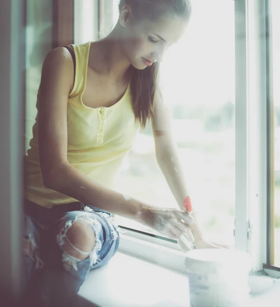 Женщина расписывает стену квартиры кистью, аккуратно оканчивая оконную раму — стоковое фото