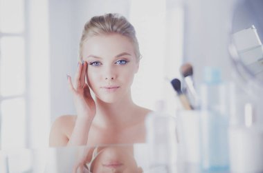 Bornozlu genç kadın banyo aynasına bakıyor.