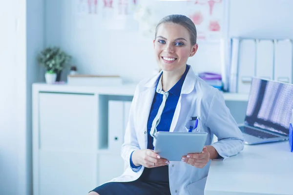Női orvos portréja a kórházi folyosón, táblagéppel a kezében, kamerába néz, mosolyog — Stock Fotó
