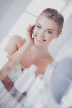 Bornozlu genç kadın banyo aynasına bakıyor.