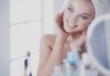 Bornozlu genç kadın banyo aynasına bakıyor.