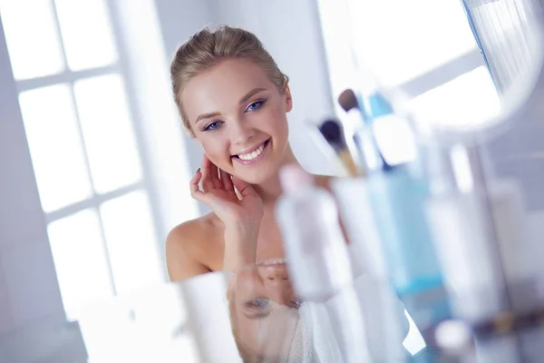 Mujer joven en albornoz mirando en el espejo del baño —  Fotos de Stock