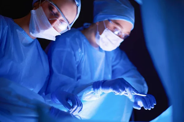 Equipo de médicos en cirugía en un fondo oscuro. — Foto de Stock