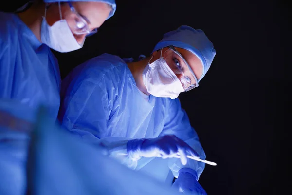 Команда врачей в хирургии на тёмном фоне. — стоковое фото