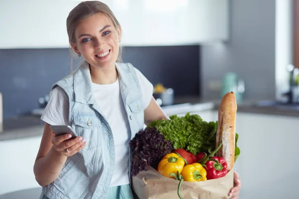 Ung kvinna som håller i matkassen med grönsaker.Står i köket — Stockfoto