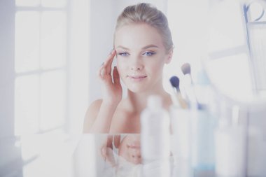 Bornozlu genç kadın banyo aynasına bakıyor.