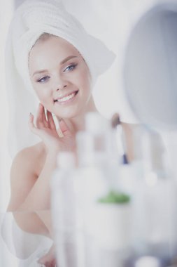 Bornozlu genç kadın banyo aynasına bakıyor.