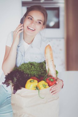 Mutfakta cep telefonu taşıyan gülümseyen bir kadın.