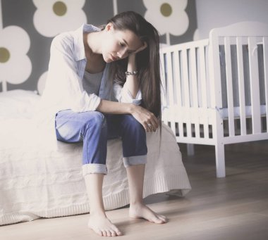 Genç çocuk karyolası yakın yatağın üstüne oturan kadın yorgun. Genç anne.