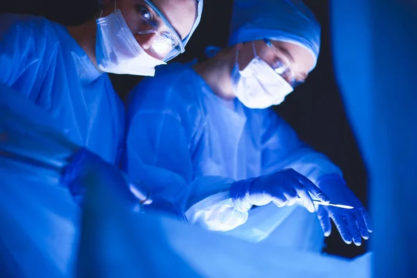 Doctors team in surgery in a dark background.