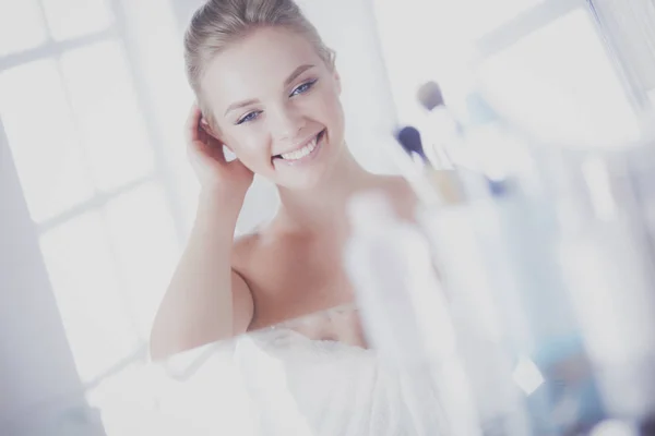 Νεαρή γυναίκα με μπουρνούζι που κοιτάζει στον καθρέφτη του μπάνιου — Φωτογραφία Αρχείου