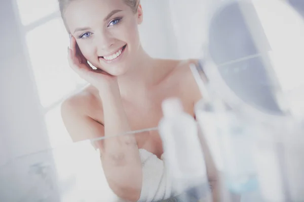 Νεαρή γυναίκα με μπουρνούζι που κοιτάζει στον καθρέφτη του μπάνιου — Φωτογραφία Αρχείου