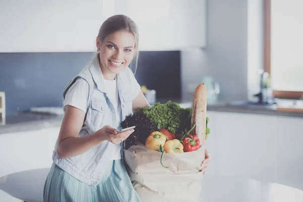 Jeune femme tenant sac d'épicerie avec des légumes. Debout dans la cuisine — Photo