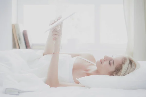 Menina segurando tablet digital com tela em branco e sorrindo para a câmera no quarto — Fotografia de Stock