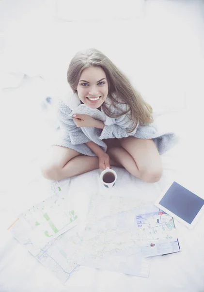 Relaxado jovem mulher sentada na cama com uma xícara de café e tablet digital — Fotografia de Stock