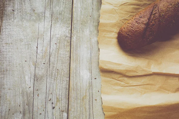 Tahta masanın üzerinde kağıda sarılı bir somun ekmek.. — Stok fotoğraf