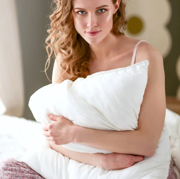 Mujer joven sosteniendo una almohada mientras está sentada en su cama . —  Fotos de Stock