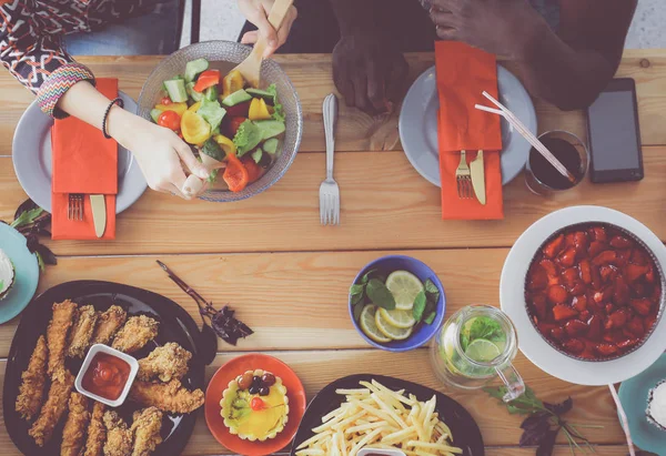 Top view of group of people having dinner together while sitting at wooden table. Food on the table. People eat fast food.