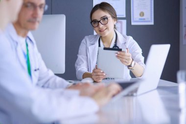 Ciddi bir tıbbi ekip parlak bir ofiste dizüstü bilgisayar kullanıyor.