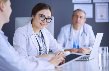 Ciddi bir tıbbi ekip parlak bir ofiste dizüstü bilgisayar kullanıyor.