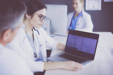 Ciddi bir tıbbi ekip parlak bir ofiste dizüstü bilgisayar kullanıyor.