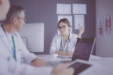 Ciddi bir tıbbi ekip parlak bir ofiste dizüstü bilgisayar kullanıyor.