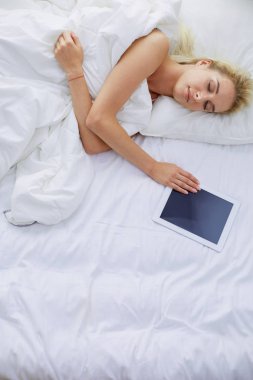 Elinde boş ekranlı dijital tablet tutan ve yatak odasında kameraya gülümseyen bir kız.