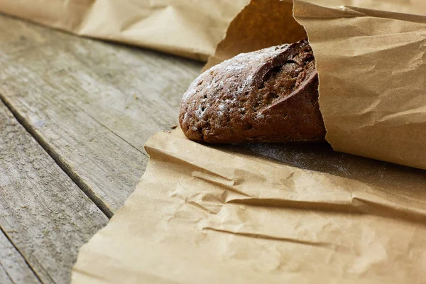Ένα καρβέλι ψωμί συσκευασμένο σε χαρτί σε ξύλινο τραπέζι. — Φωτογραφία Αρχείου