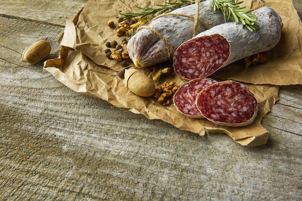 Italian salami wih sea salt, rosemary, garlic and nuts on paper. Rustic style. Top view.